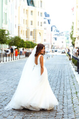 Fototapeta premium Young elegant bride in a white dress in the city. Beautyful bride with luxury make-up and hairstyle. Happy newlywed woman. Smiling bride. Wedding day. Fashion bride.