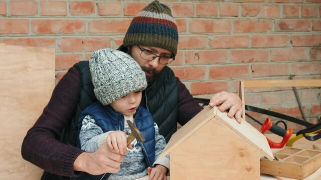 Handheld shot: Young caucasian father and his little son working together, building a wooden bird feeder