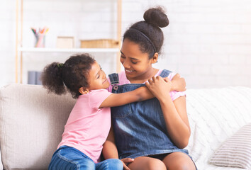 Cheerful african sisters embracing on couch at home