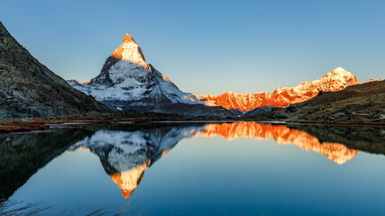 Classical Swiss view of snow-capped epic Mattergorn mountain peak reflected in Riffelsee lake. Iconic landmark in Switzerland located near Zermatt resort. Picturesque landscape of alpenglow in Alps. - obrazy, fototapety, plakaty