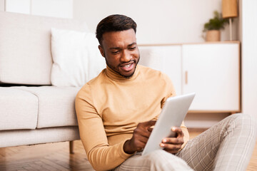 Afro Man Using Digital Tablet Sitting On Floor At Home