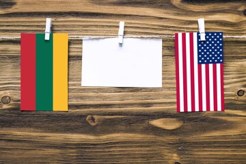 Hanging flags of Lithuania and United States attached to rope with clothes pins with copy space on white note paper on wooden background.Diplomatic relations between countries.