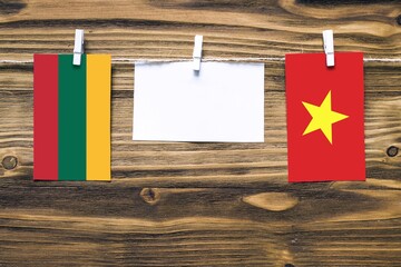 Hanging flags of Lithuania and Vietnam attached to rope with clothes pins with copy space on white note paper on wooden background.Diplomatic relations between countries.