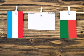 Hanging flags of Luxembourg and Madagascar attached to rope with clothes pins with copy space on white note paper on wooden background.Diplomatic relations between countries.