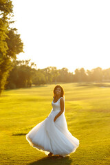 Fototapeta na wymiar Happy beautiful young bride outside on a summer meadow at the sunset. Luxury elegant bride in a white dress at the sunset. Beautyful bride with luxury make-up and hairstyle. Wedding day.
