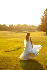 Fototapeta na wymiar Happy beautiful young bride outside on a summer meadow at the sunset. Luxury elegant bride in a white dress at the sunset. Beautyful bride with luxury make-up and hairstyle. Wedding day.