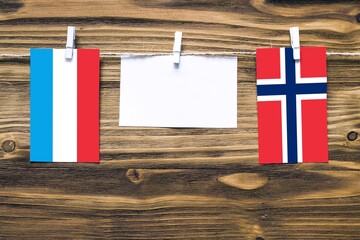 Hanging flags of Luxembourg and Norway attached to rope with clothes pins with copy space on white...
