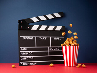 Cinema concept. Movie clapper and fly caramel popcorn on blue and red background.