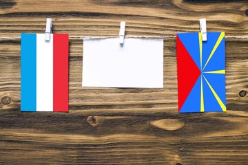 Hanging flags of Luxembourg and Reunion attached to rope with clothes pins with copy space on white...