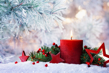 Christmas or advent candle, fir branches, berry and red stars in snow against beautiful winter...