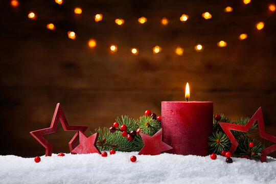 Christmas or advent candle, fir branches, berry and red stars in snow against light  garland background. Holiday card.