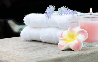 Closeup clean towels with pink candle and flower on wooden table, black background. Copy space.
