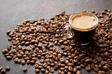 Coffee beans, metal scoop and a glass cup of espresso on a dark brown background.