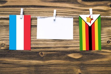Hanging flags of Luxembourg and Zimbabwe attached to rope with clothes pins with copy space on...