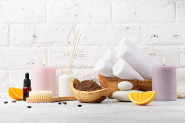 Spa and relax. Orange and coffee scrub, stones, towels and brush for body on white wall background.