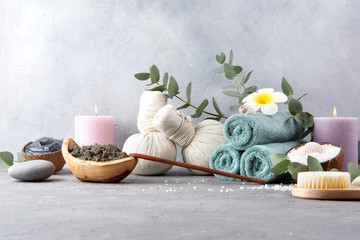 Beautiful spa and relax concept. Green tea scrub, dead sea mud, cotton pouches with herbs for massage, sea stones, eucalyptus and other Spa accessories on grey table.
