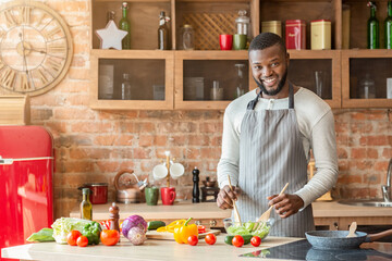 Smiling black man preparing fresh healthy salad at kitchen