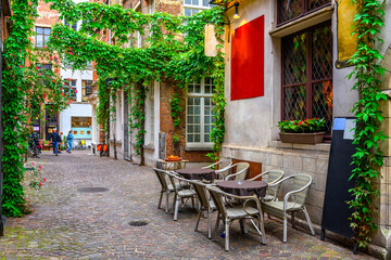 Fototapeta na wymiar Old street with tables of cafe in historic city center of Antwerpen (Antwerp), Belgium. Cozy cityscape of Antwerp. Architecture and landmark of Antwerpen