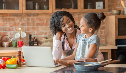 Mommy and daughter embracing, reading recipe on laptop at kitchen