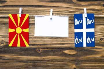 Fototapeta premium Hanging flags of Macedonia and Martinique attached to rope with clothes pins with copy space on white note paper on wooden background.Diplomatic relations between countries.