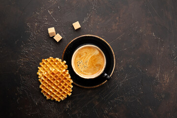Obraz na płótnie Canvas Fresh coffee in black mug with plate, sugar and traditional Belgian sponge waffles on dark brown background top view