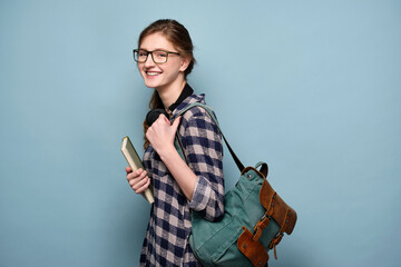 Fototapeta na wymiar Laughing girl in a plaid shirt and glasses on a blue background with a book and a backpack.