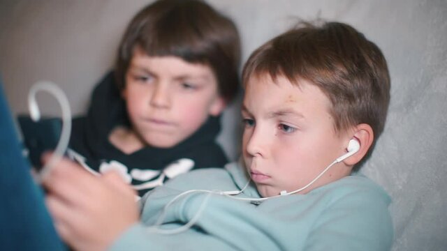 Two boys use a smartphone while sitting at home.