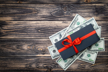 Black gift box with bow with dollars banknotes on wooden backgroung. top view