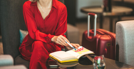 Cropped portrait of gorgeous lady with blonde hair wearing red jumpsuit, looking at notes in her notebook while sitting on the couch. Successful beautiful woman concept. Horizontal shot. Front view