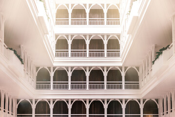 Horizontal shot of bright spacious lobby interior. It consists of many white arches. Balcony design...