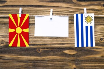 Hanging flags of Macedonia and Uruguay attached to rope with clothes pins with copy space on white...