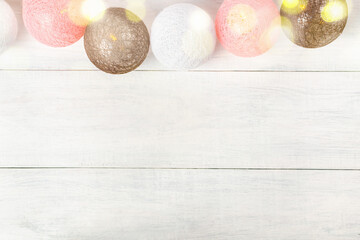 Garland of balls made of threads with yellow bokeh lights on white wooden planks. Beautiful cozy romantic light background for holiday cards and invitations, for handmade masters.