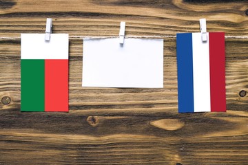 Hanging flags of Madagascar and Netherlands attached to rope with clothes pins with copy space on white note paper on wooden background.Diplomatic relations between countries.