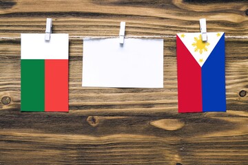 Hanging flags of Madagascar and Philippines attached to rope with clothes pins with copy space on white note paper on wooden background.Diplomatic relations between countries.