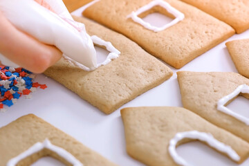 Woman's hands decorate with sugar sweet cookies for gingerbread houses. Cooking homemade gingerbread house