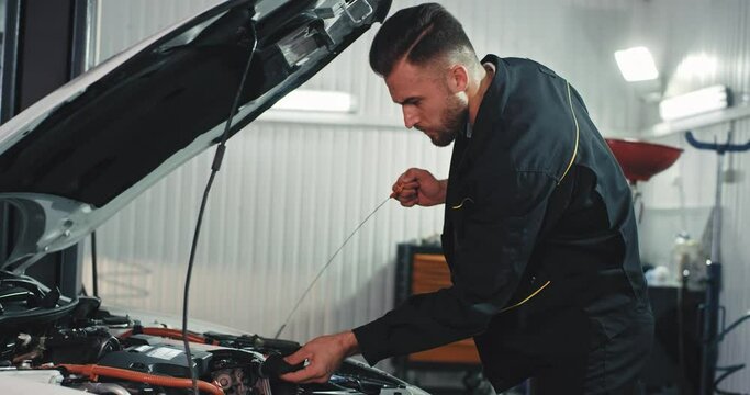 Good looking mechanic guy in a modern service auto checking carefully the oil level from the car