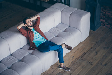 High angle above view photo of handsome guy in high spirits holding hands behind head sitting couch...