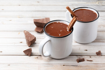 Hot chocolate in two white metall mugs with cinnamon