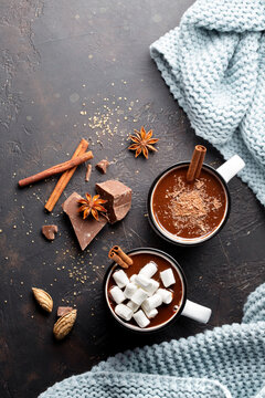 Hot chocolate in white metall mug with marshmallow and cinnamon stick on brown background top view