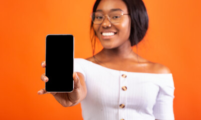 Fototapeta premium Black Girl Showing Phone Empty Screen Standing, Orange Background, Mockup
