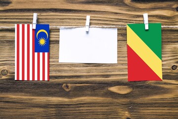 Hanging flags of Malaysia and Republic Of The Congo attached to rope with clothes pins with copy space on white note paper on wooden background.Diplomatic relations between countries.