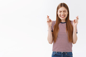 Anxious hopeful young fair-haired caucasian girl in striped t-shirt praying, clench teeth nervously close eyes and cross fingers good luck, anticipating something important, nervously awaiting