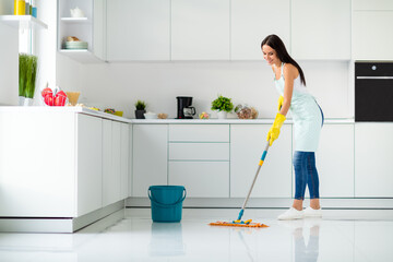 Profile side full size photo of positive cheerful girl having mop washing floor wearing white singlet yellow rubber gloves dotted apron fell content enjoy household chores in kitchen house indoors