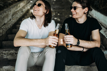 Two Stylish Twins Brothers Having Fun Drinking Beer on the Stairs
