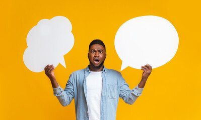 Confused black guy holding two speech bubbles on yellow background - obrazy, fototapety, plakaty