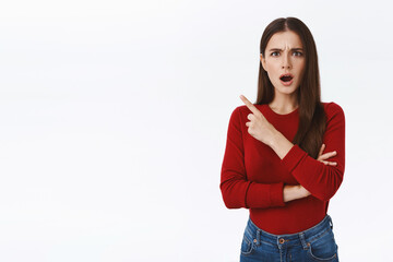 Shocked dissatisfied pretty, feminine brunette girl in red sweater looking concerned and disappointed, gasping open mouth displeased, pointing upper left corner, frowning frustrated and upset