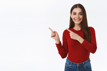 Friendly, assertive pretty brunette girl gladly showing customer promo, good offer, pointing upper left corner, smiling happy, helping out person who asking for direction, standing white background