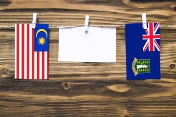 Hanging flags of Malaysia and British Virgin Islands attached to rope with clothes pins with copy space on white note paper on wooden background.Diplomatic relations between countries.