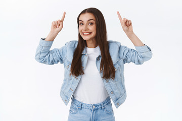 Excited, funny and pretty brunette caucasian female in denim jacket, jeans, pointing fingers up...