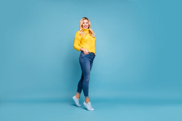 Full length photo of amazing blond lady slim perfect shapes street autumn look hold hands in pockets wear knitted yellow pullover jeans isolated blue color background